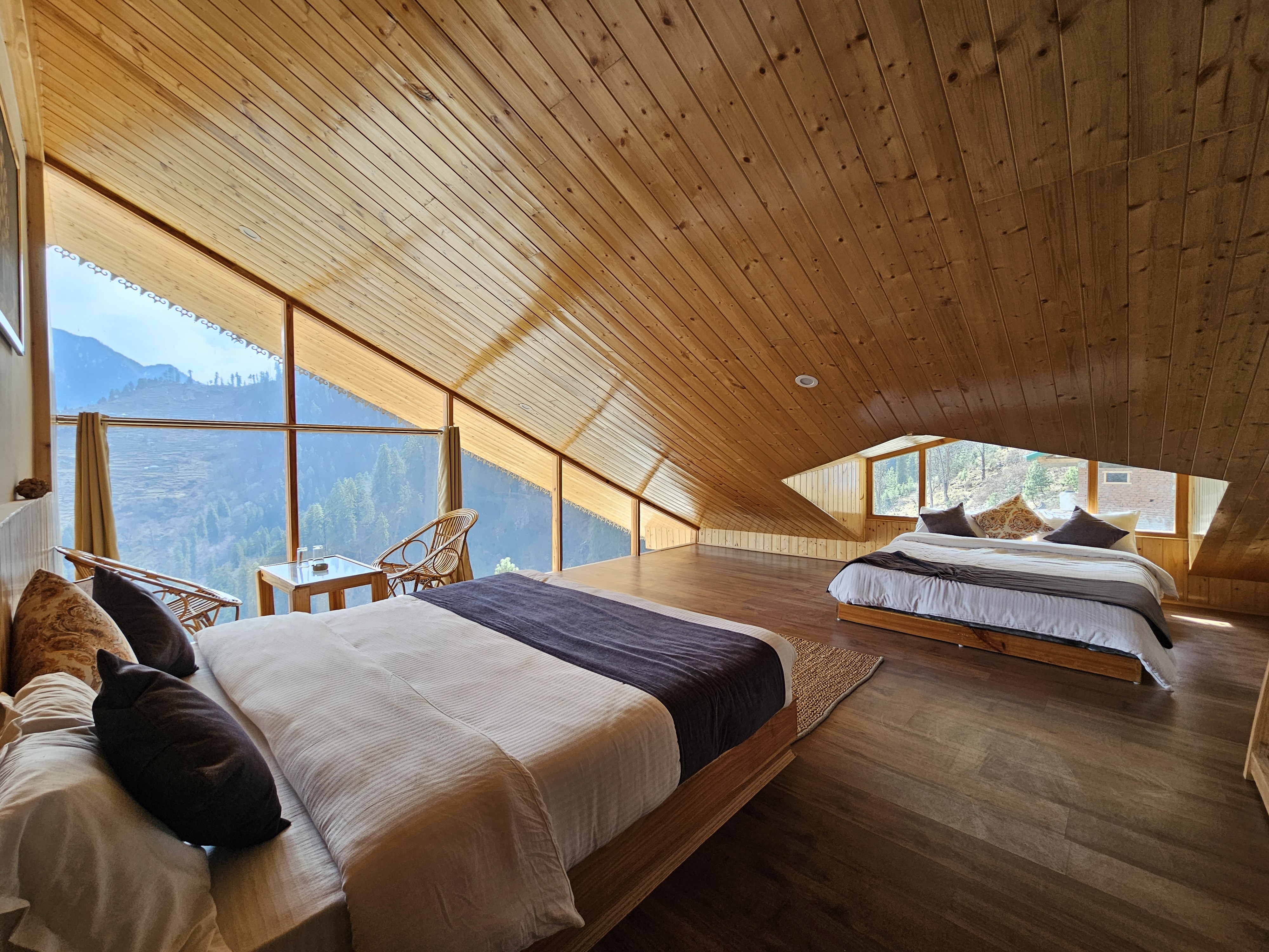 Twin attic room with two beds under a high pine ceiling and a glass wall facing the valley